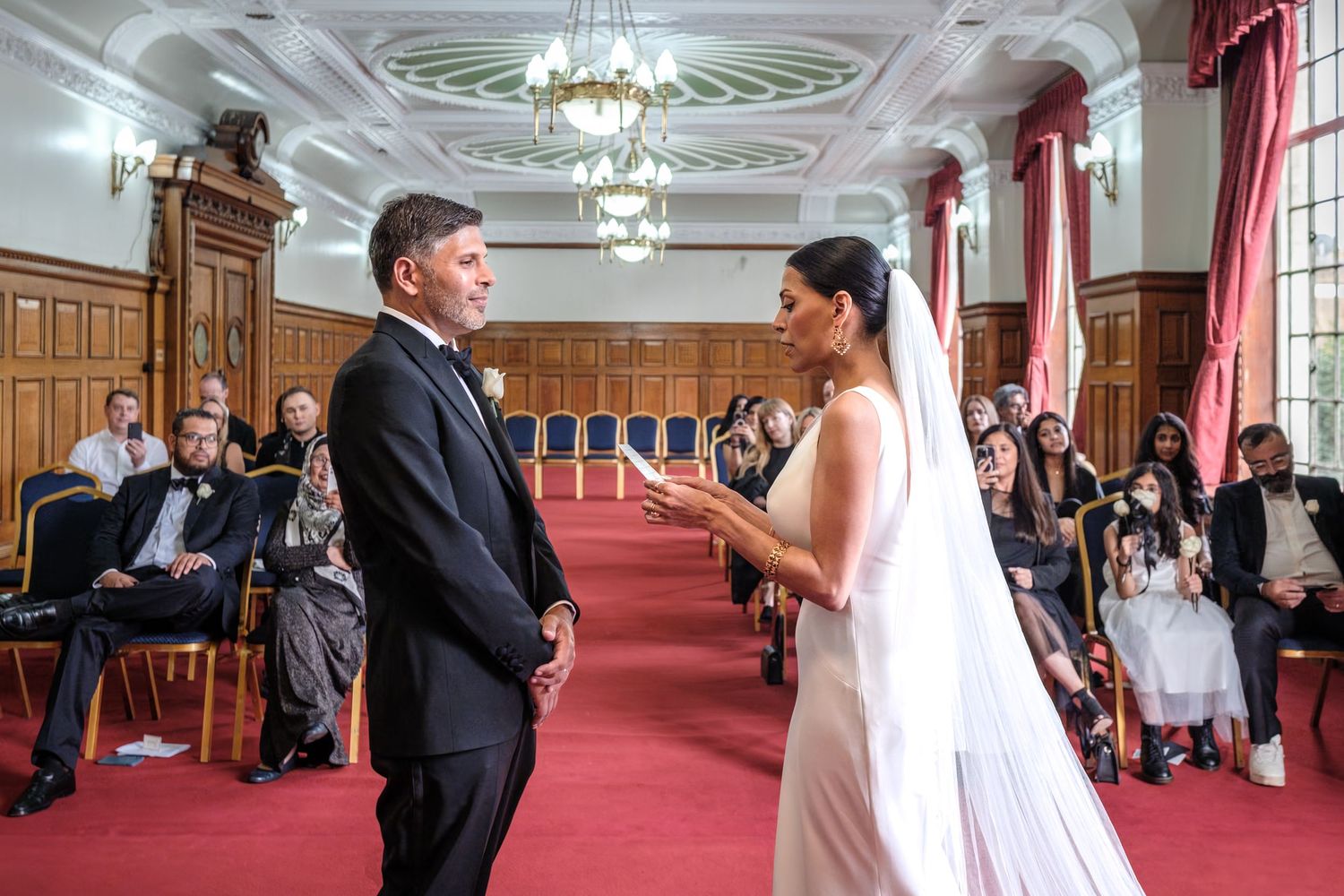 A bride and groom stand together in a grand, ornate hall during their wedding ceremony.