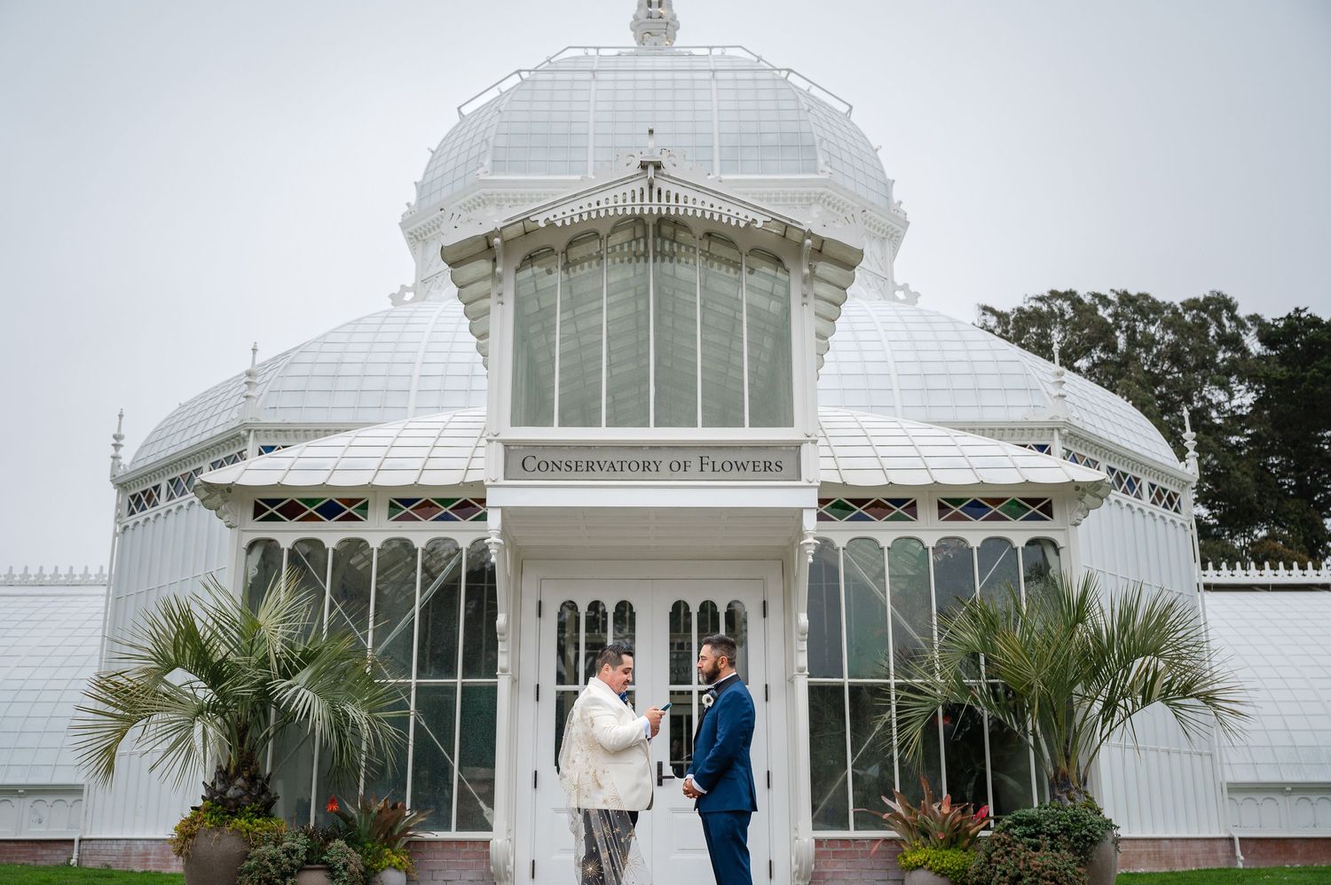 A romantic wedding couple shares intimate moments in a garden setting with wooden fence and lush greenery backdrop.
