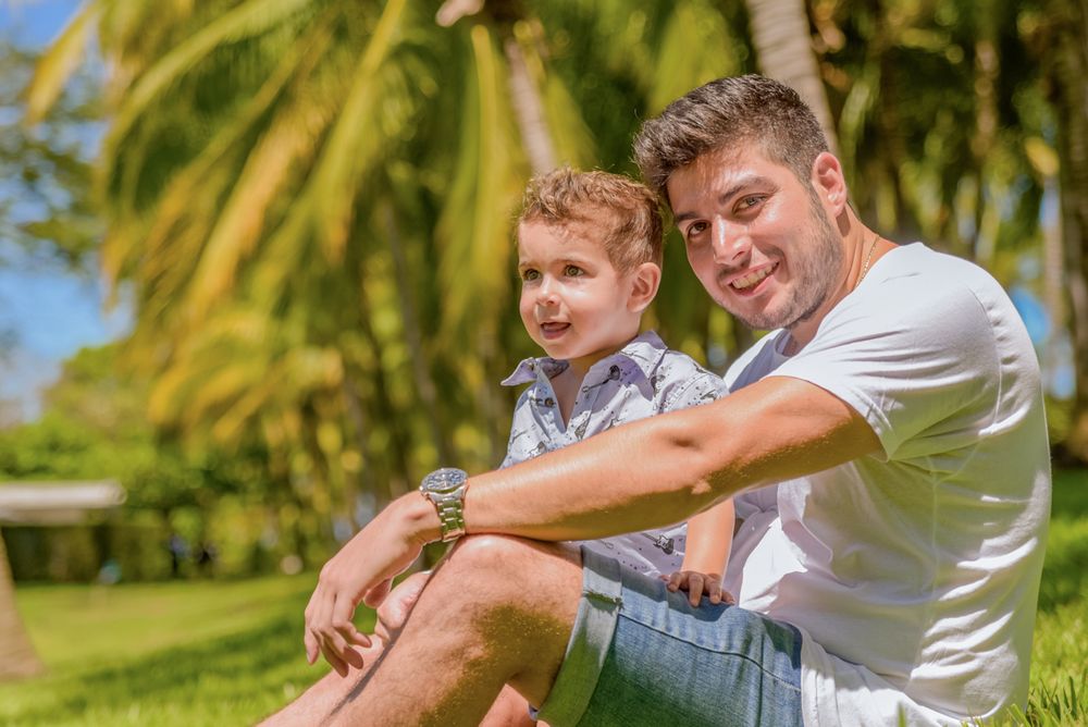 Two people sit together outdoors on a sunny day with palm trees visible in the background.