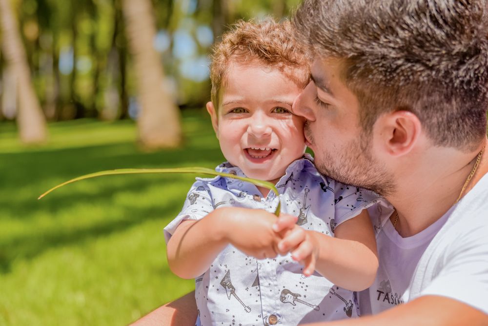 A parent and child share a joyful moment together while sitting outdoors on a sunny day in a grassy area.