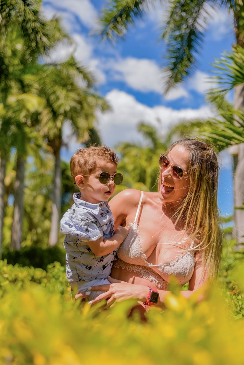 A joyful moment captured between a woman and young child playing together among palm trees and yellow flowers on a sunny day.