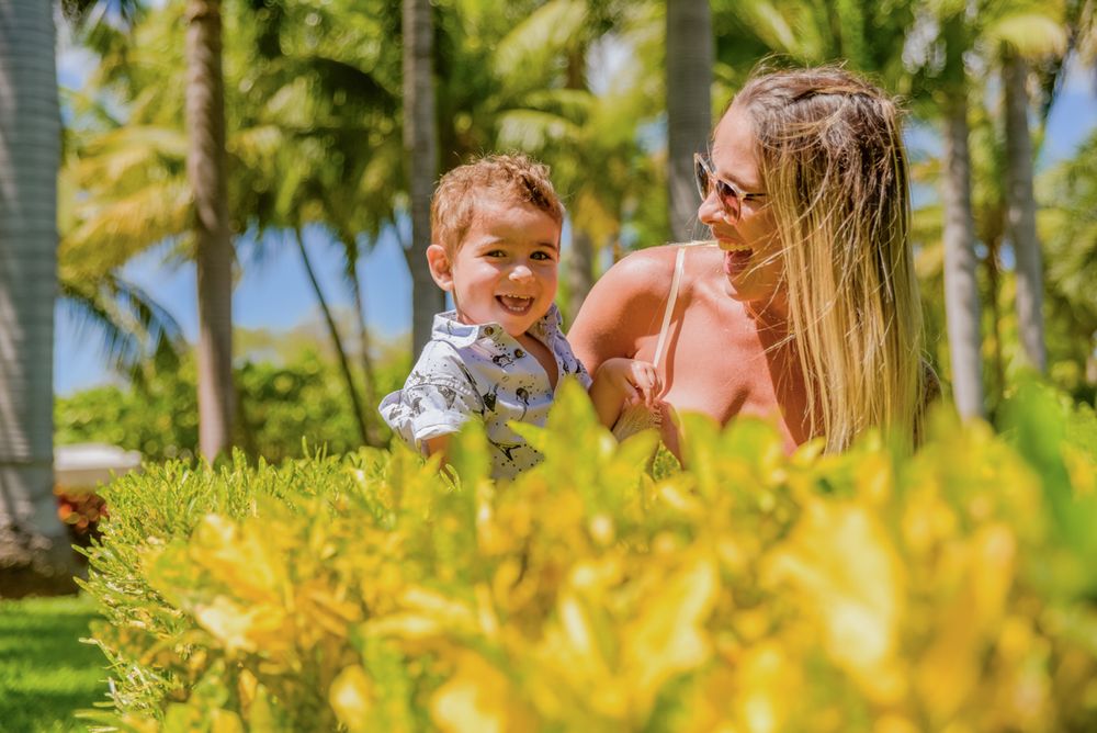 Family enjoying a sunny day together in a lush garden with palm trees and vibrant yellow flowers in the foreground.