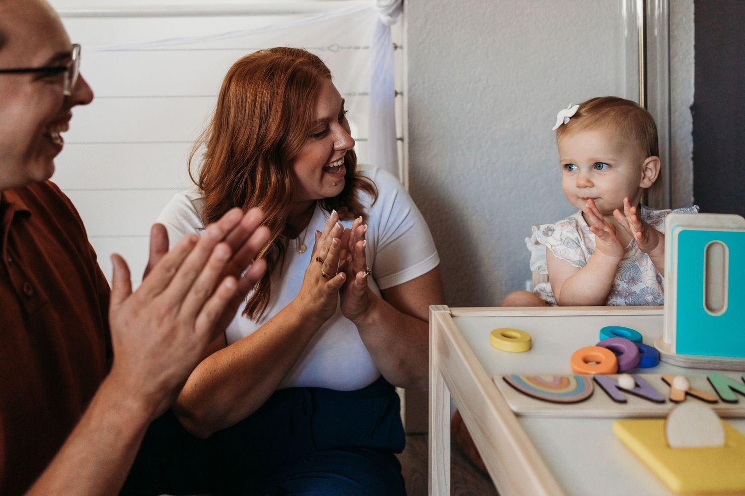 Family sharing meal together at dining table with toddler in highchair while playing peek-a-boo.