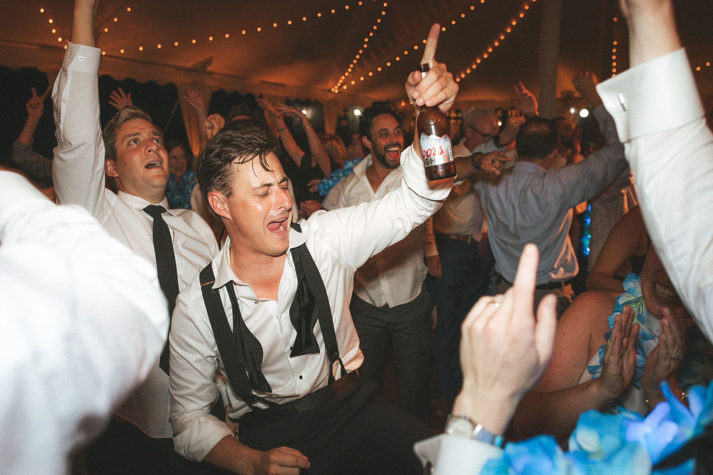A lively dance party scene with people raising their hands and dancing under string lights at a celebration.