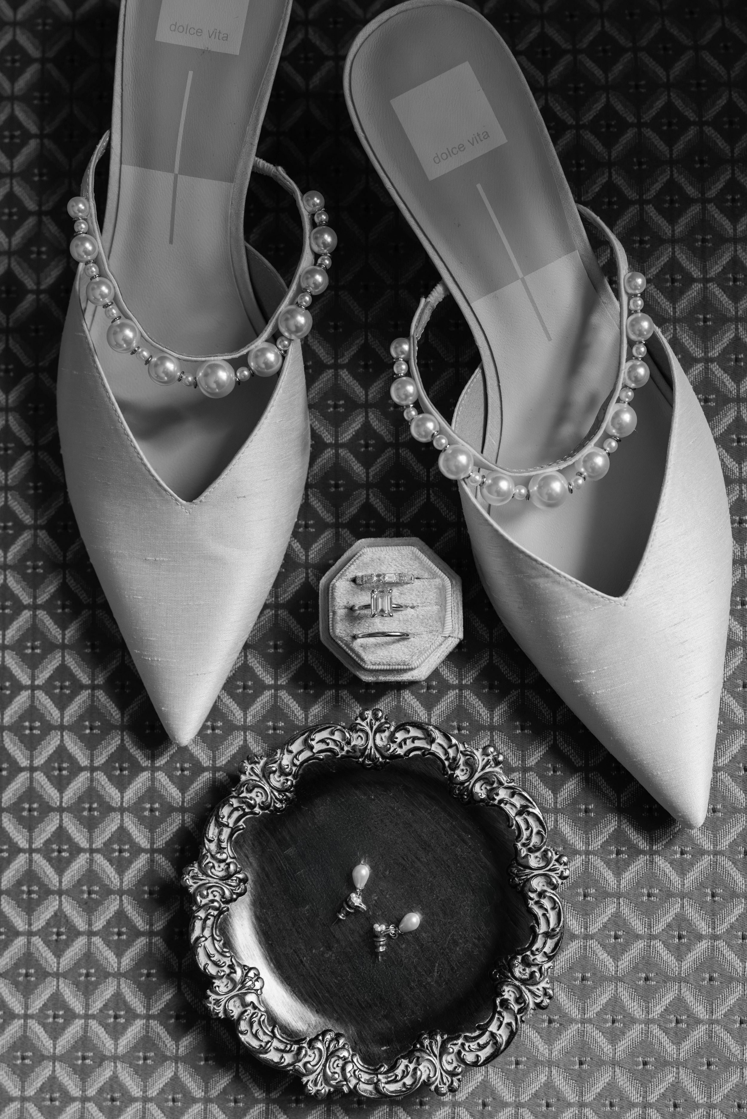 Elegant white pointed-toe shoes with rhinestone embellishments arranged in a row against a patterned background.
