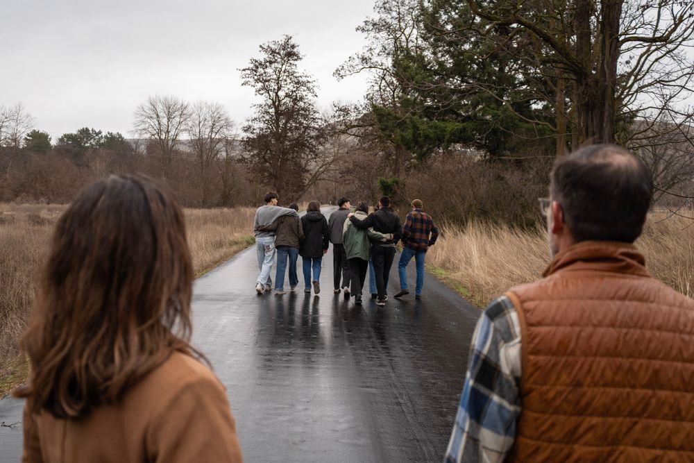 Two people watch a group walking away on a wet rainy road surrounded by dormant winter trees.