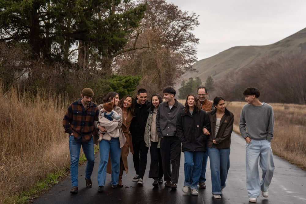 A group of ten people walk together on a path surrounded by autumn foliage and rolling hills.