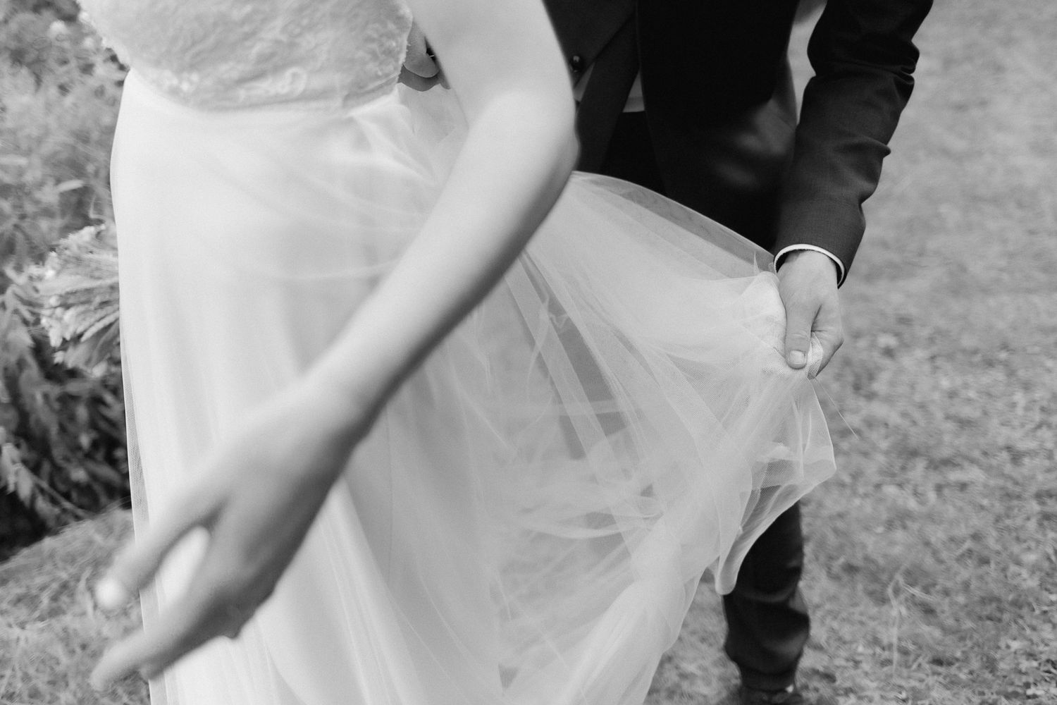 Black and white close-up detail of delicate tulle wedding dress fabric being adjusted outdoors.