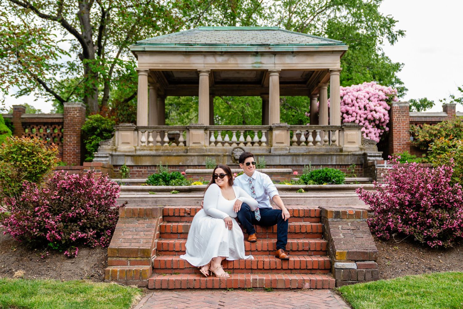 LGBTQ+ couple sitting on steps at Lynch Park in Beverly, MA, surrounded by blooming azaleas in a formal garden.