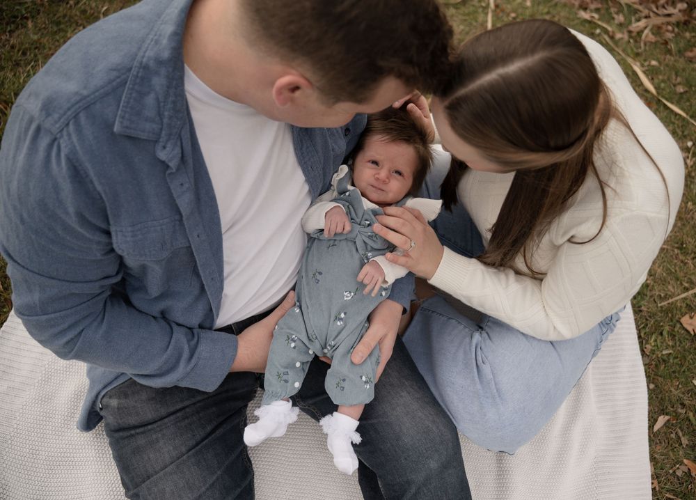 Parents lovingly gaze at their newborn baby during an outdoor family photo session.