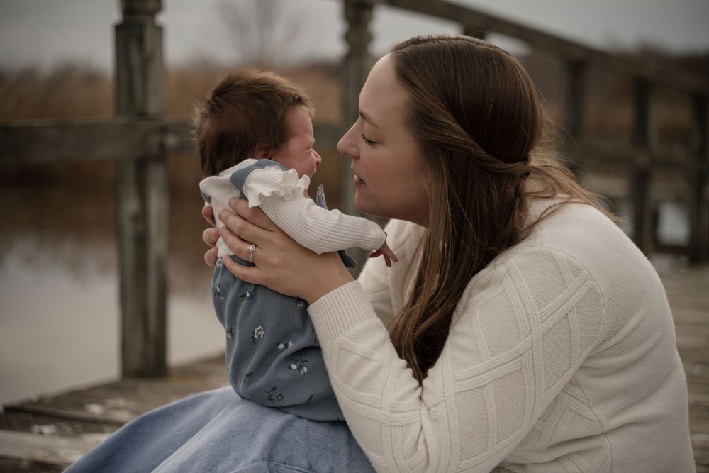 A mother lovingly gazes at her wide-eyed newborn baby on a dock.