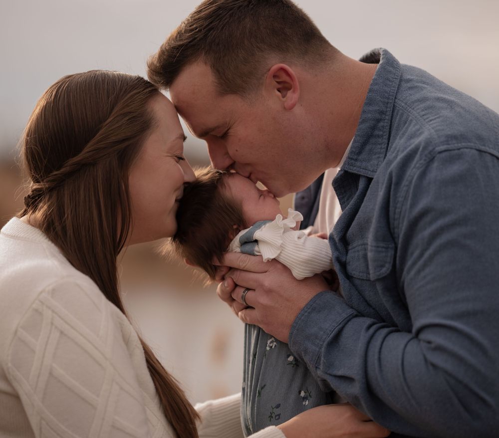 New parents tenderly kiss their sleeping newborn baby together.