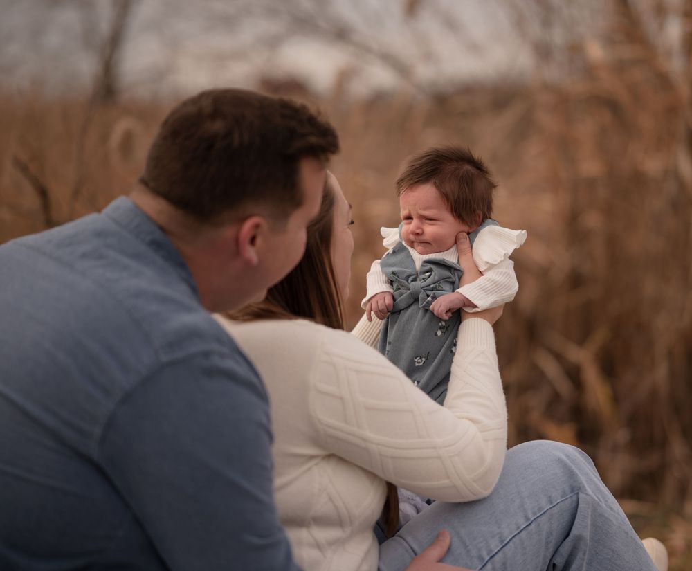 Parents holding a fussy crying baby outdoors in a natural setting during a family photo session.