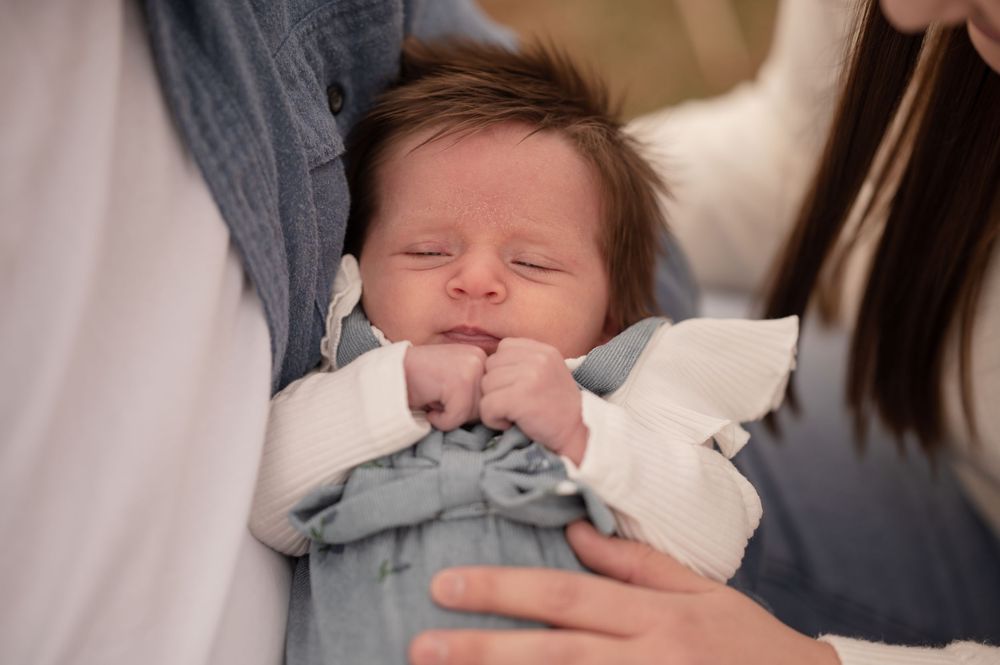 Peaceful newborn baby in a gray outfit resting with eyes closed in a parent's arms.