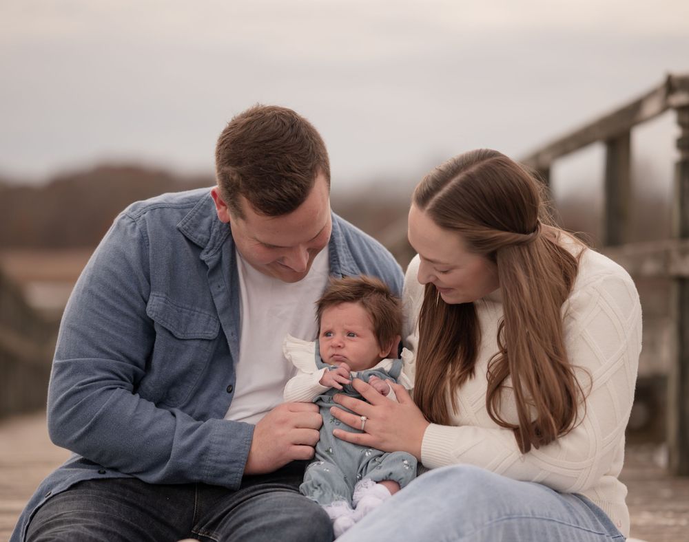 Young couple sitting outdoors admiring their newborn baby, sharing a tender family moment.