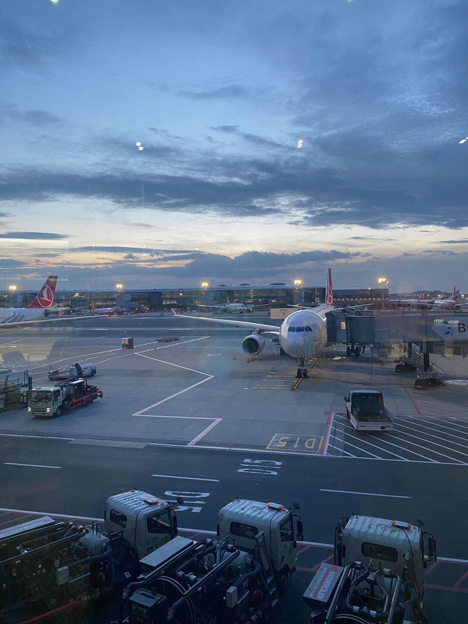Airport tarmac at dusk with parked aircraft and ground equipment visible against a dramatic blue evening sky.