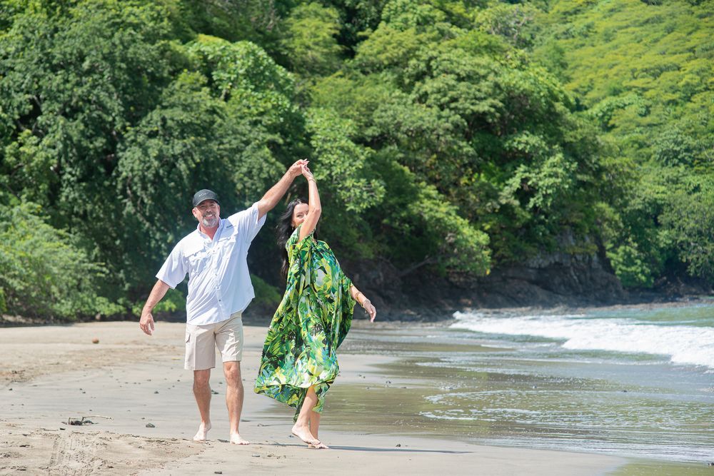 Two people walking along a tropical beach shoreline surrounded by lush green vegetation and crystal clear waters.
