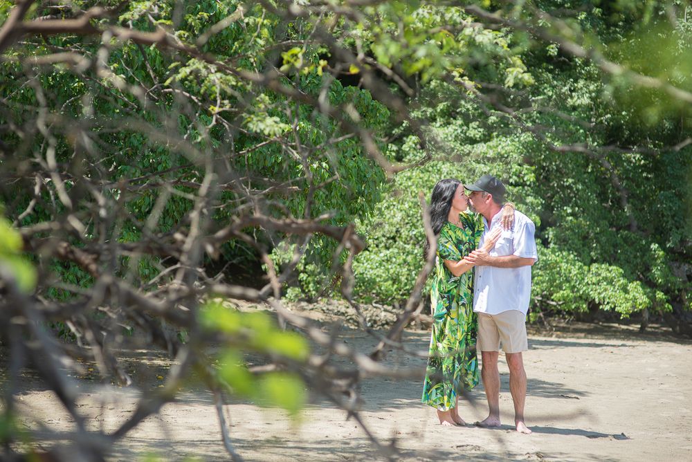 Couple walking along a lush tropical path surrounded by green foliage and trees.