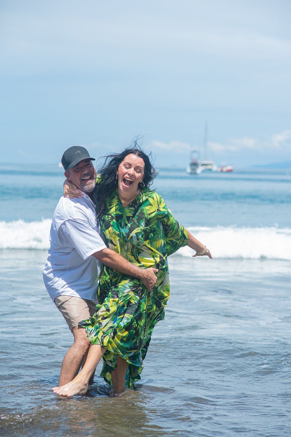 Two people play and splash in the ocean waves wearing colorful tropical clothing on a sunny beach day.