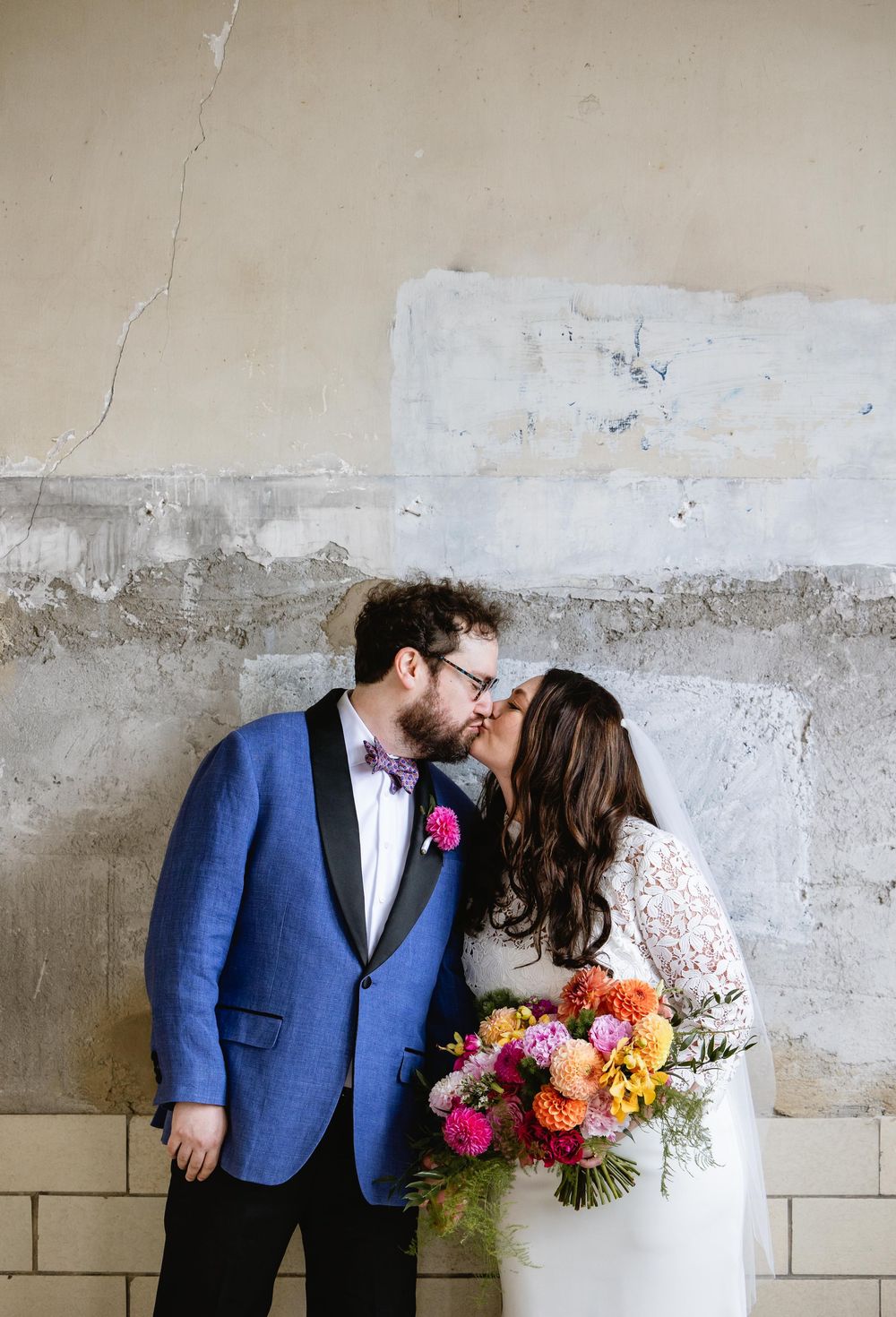 Romantic wedding moment against concrete wall with bright floral bouquet and blue suit details. Bok Building Philadelphia