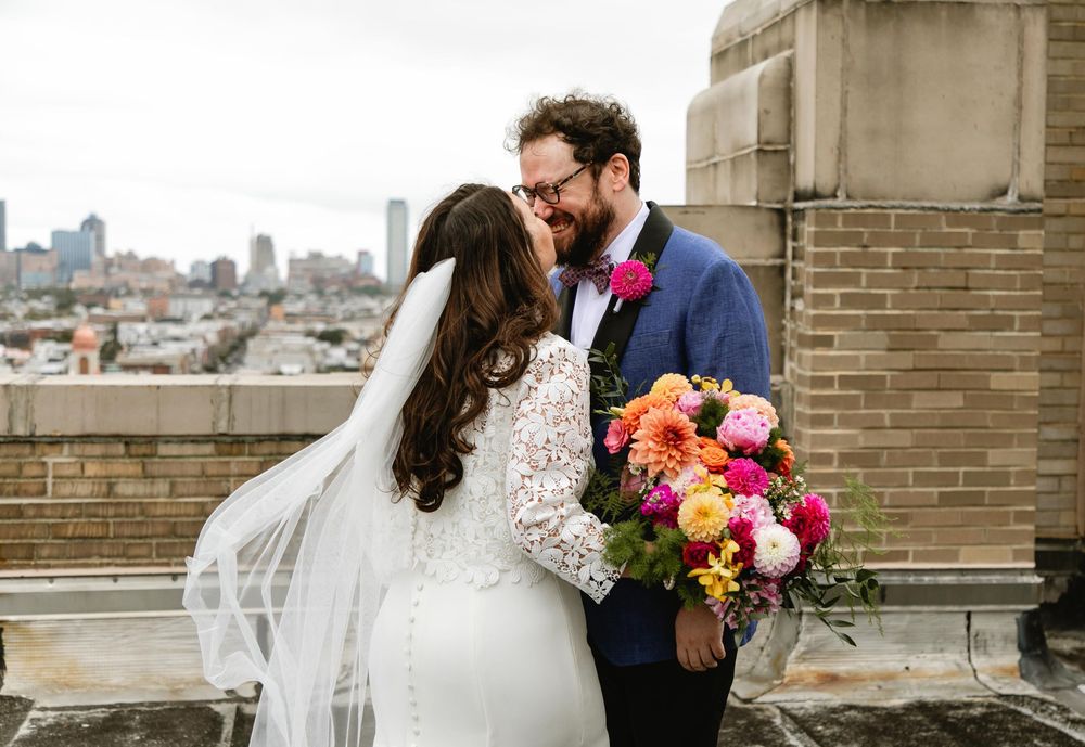 Wedding couple posing with colorful bouquet against brick wall and city views. Bok Building Philadelphia