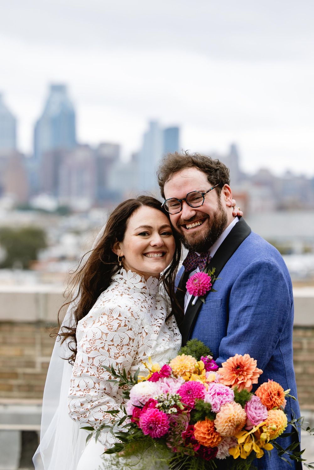 A romantic wedding moment captured on a rooftop with colorful flowers and the city skyline in the background. Bok Building Philadelphia