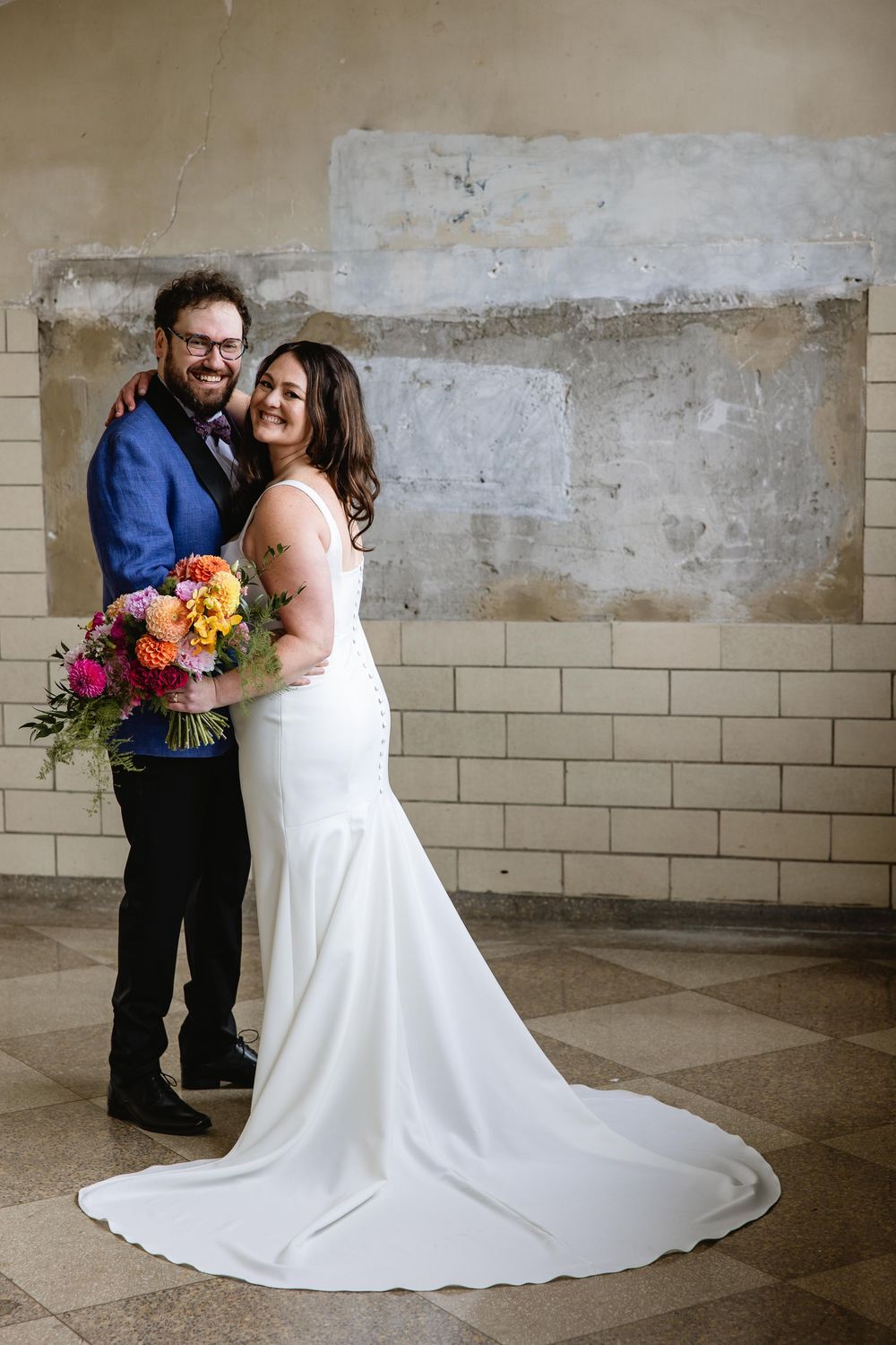 Wedding couple shares intimate moment against industrial wall with flowing white dress. Bok Building Philadelphia