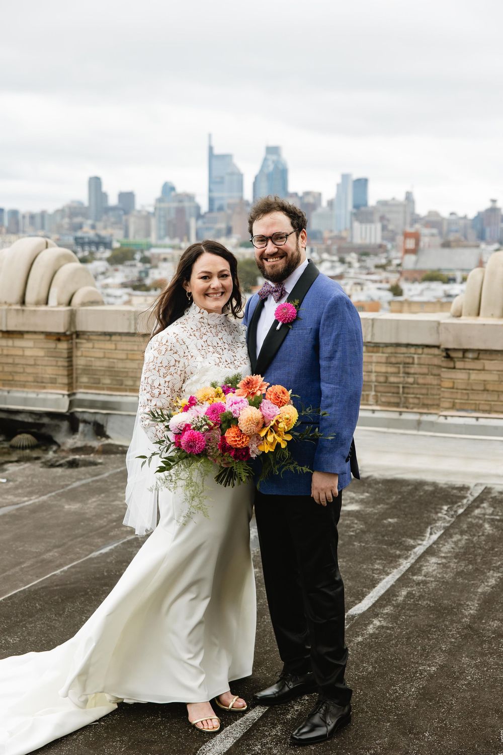 Wedding couple laughing together on rooftop with downtown skyline and bright floral arrangement. Bok Building Philadelphia