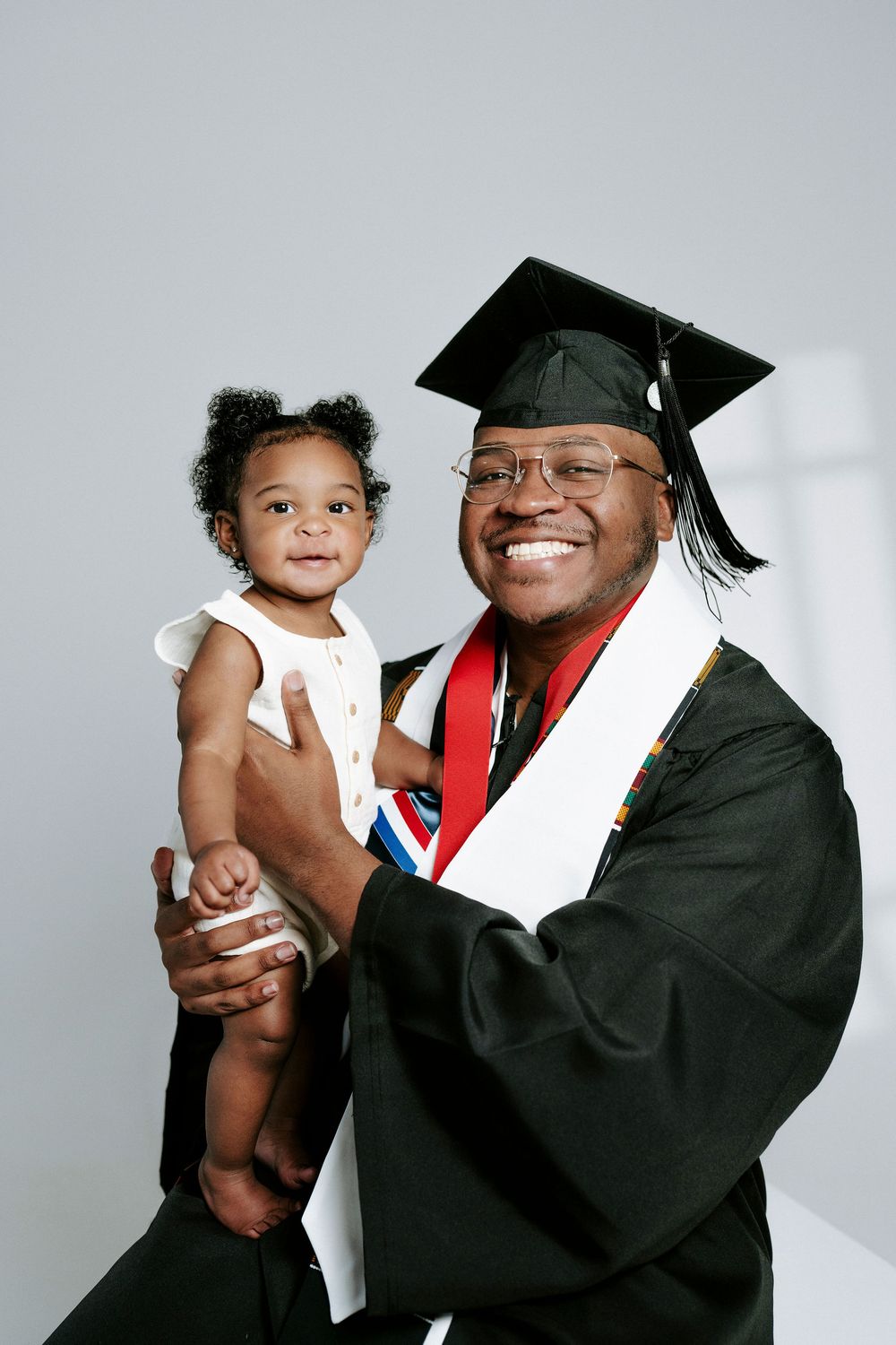 A graduate in academic regalia poses with a small child for a series of celebratory photos.