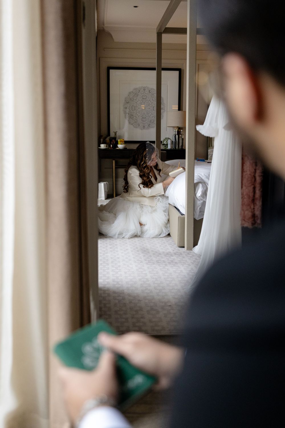 A person aims a green Nintendo Wii remote controller at a white bed in a dimly lit hotel room.