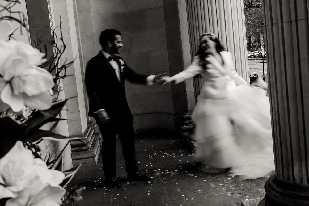 A joyful dancing moment captured in black and white at a wedding with white floral decorations and classical columns.