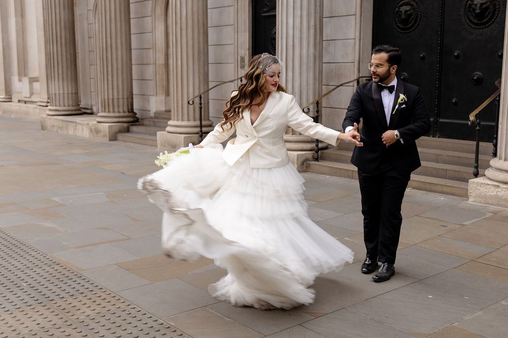 A couple twirls together in an elegant dance pose outside a historic building with columns.