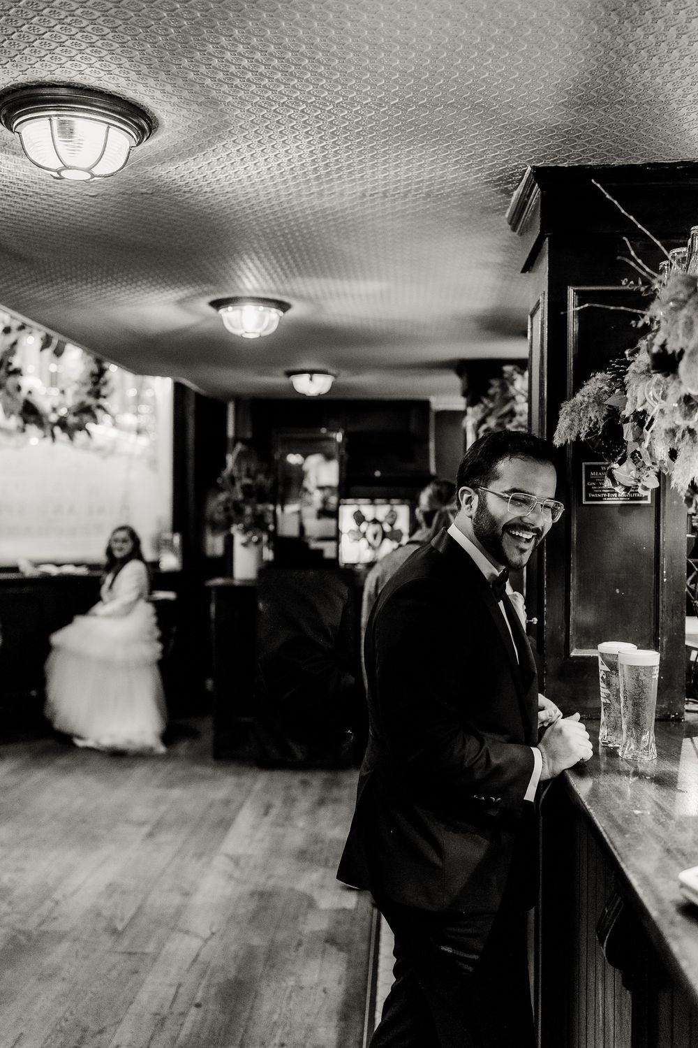 Black and white wedding reception photos showing guests celebrating at a bar in an indoor venue.