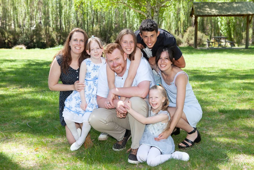 Happy family relaxing together on grass under willow trees in a park setting.