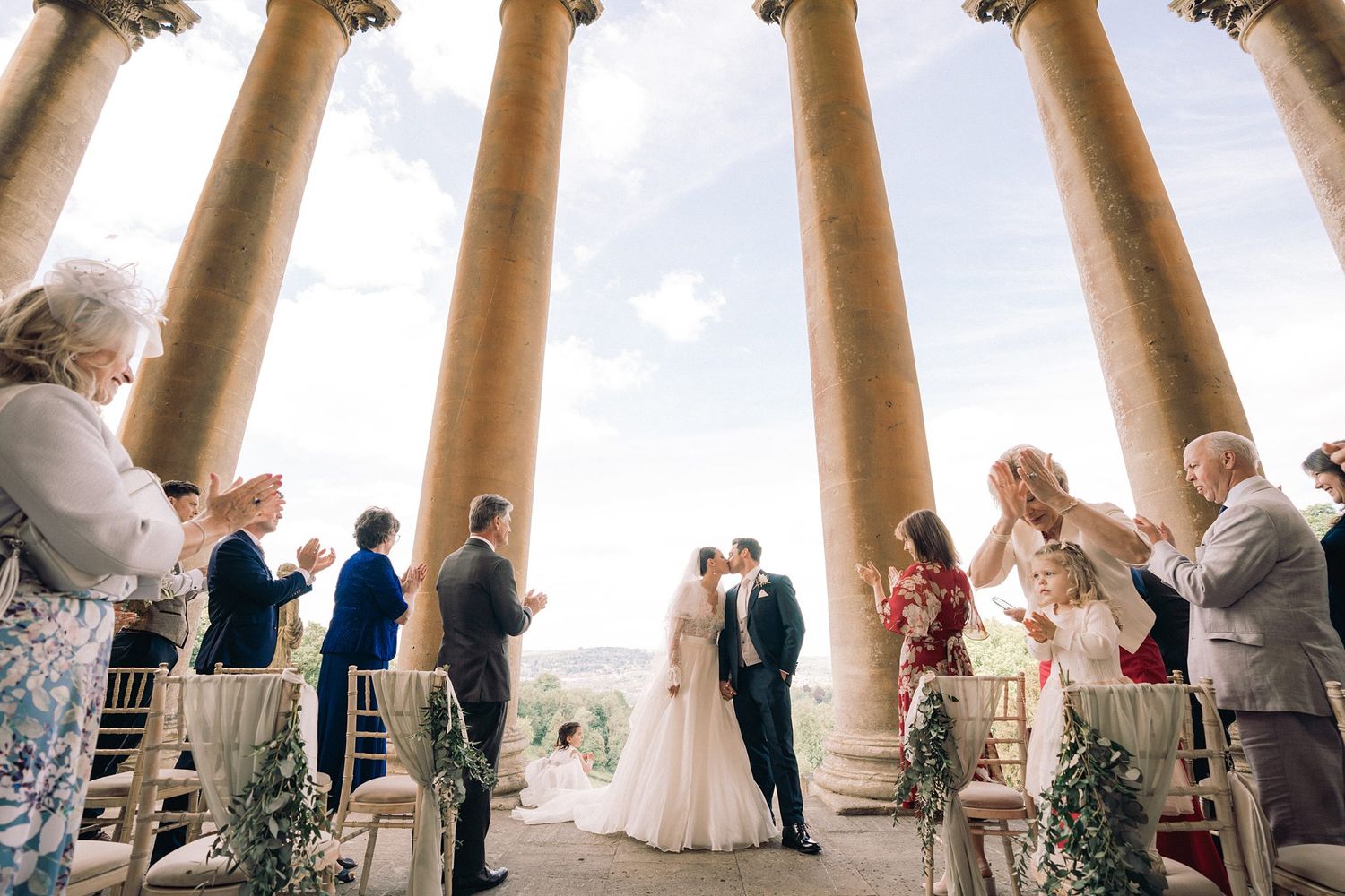 A panoramic collage of wedding ceremony moments under arched architectural columns with ocean views in the background.