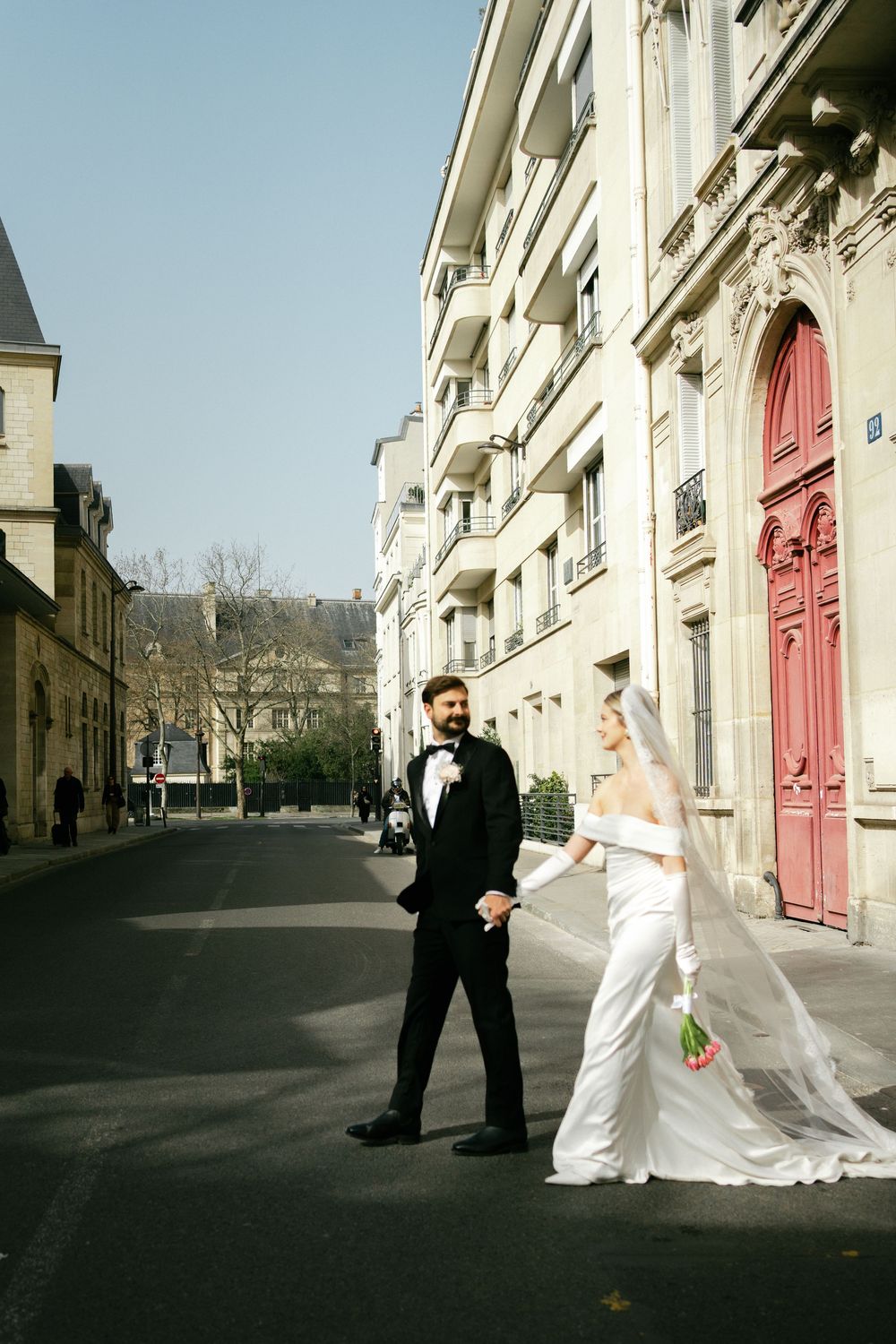 Wedding couple shares romantic moments in an elegant European-style street with classic architecture and red doors.