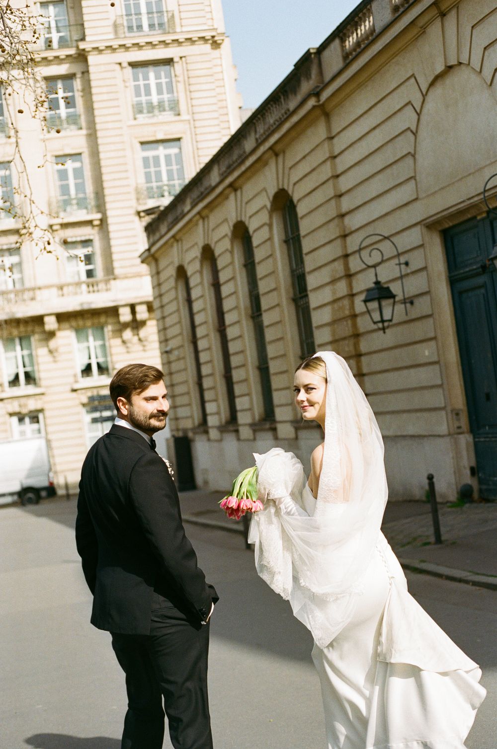 A bride and groom share a playful moment on a European cobblestone street with classic architecture in the background.