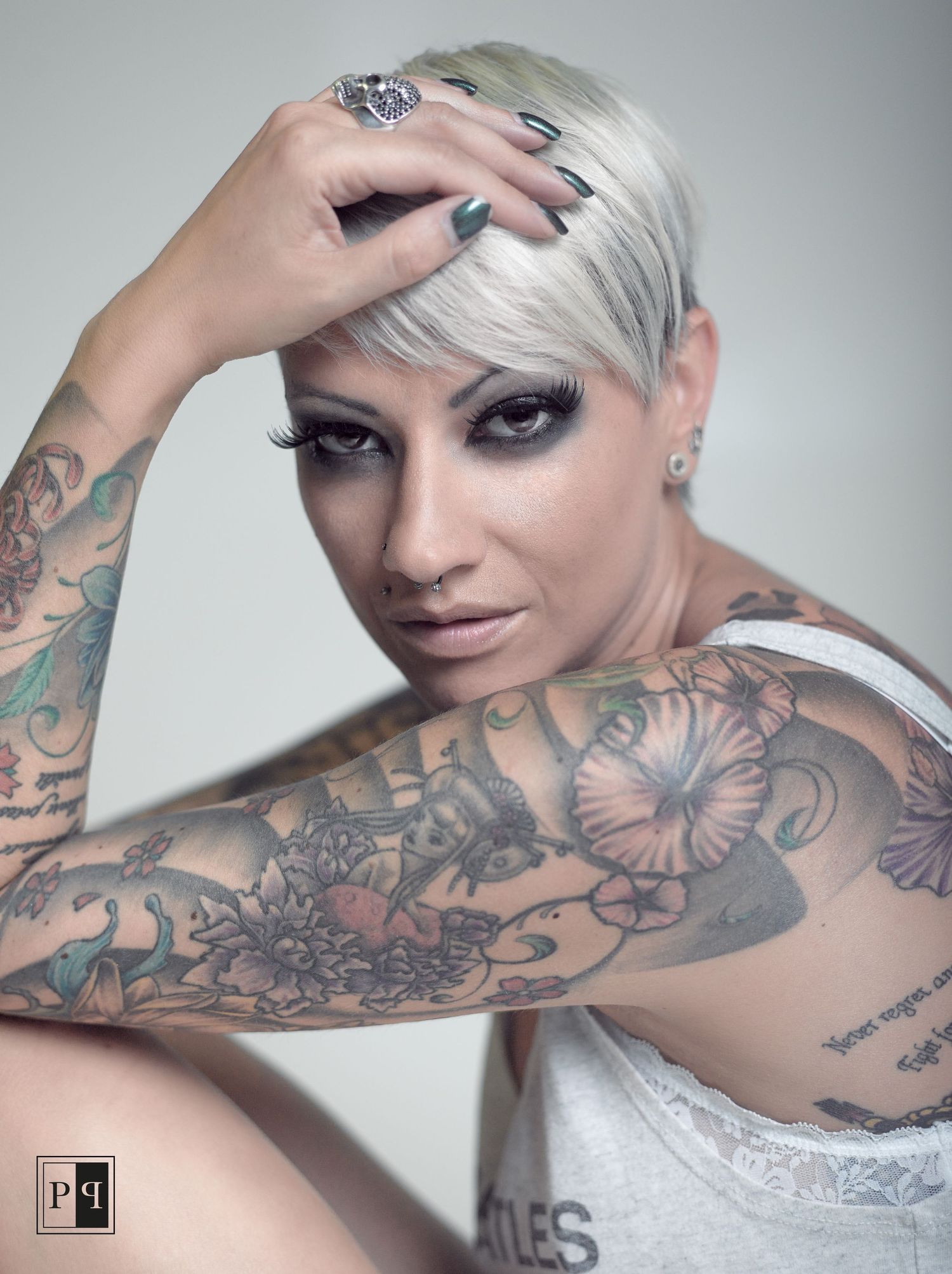 Heavily tattooed woman with platinum blonde pixie cut and dark makeup in studio portrait.