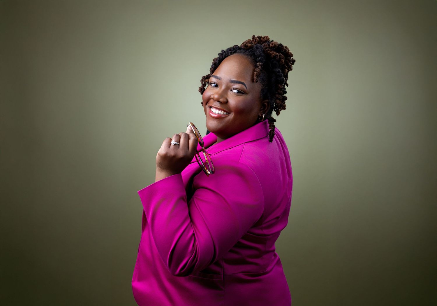Professional portrait against purple backdrop showing confident pose in bright orange blazer and white top.