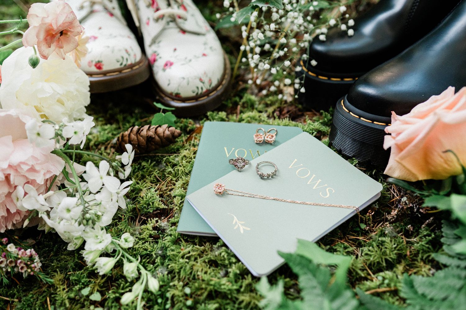 Wedding details with mint invitations, rings, floral decor, and Doc Marten boots arranged on moss