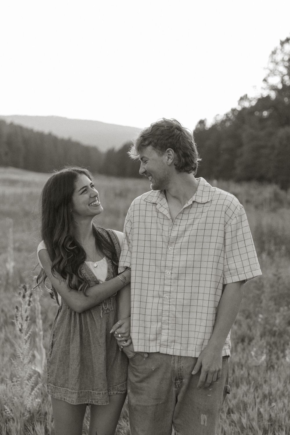 A couple shares joyful laughter together while standing in a grassy meadow on a sunny afternoon.
