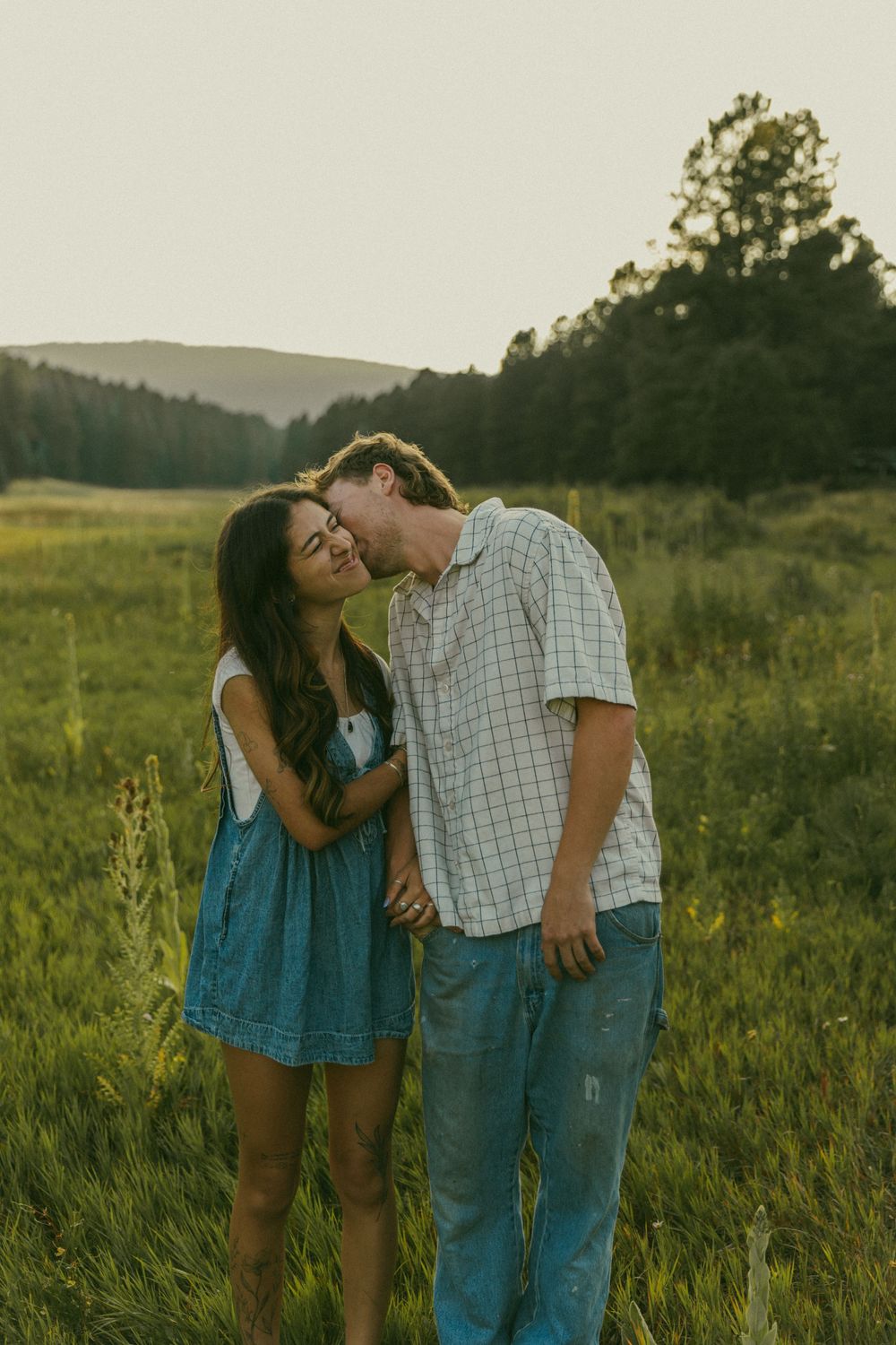 A couple shares tender moments in a sunlit meadow wearing casual summer attire.