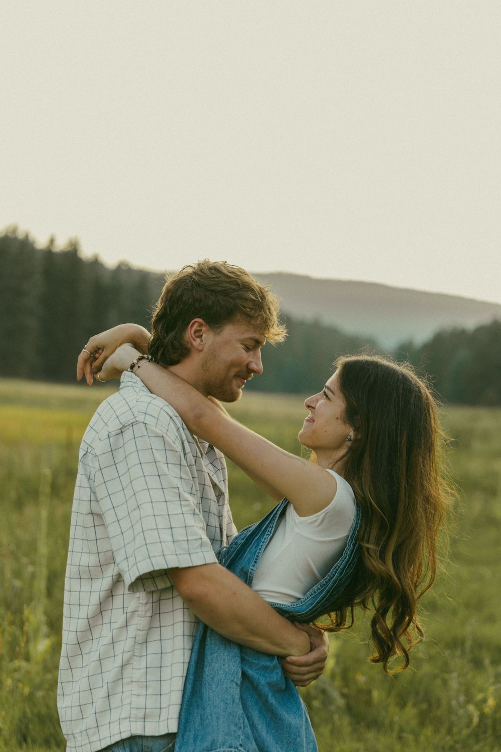 A couple shares an intimate embrace while standing in a golden field at sunset.