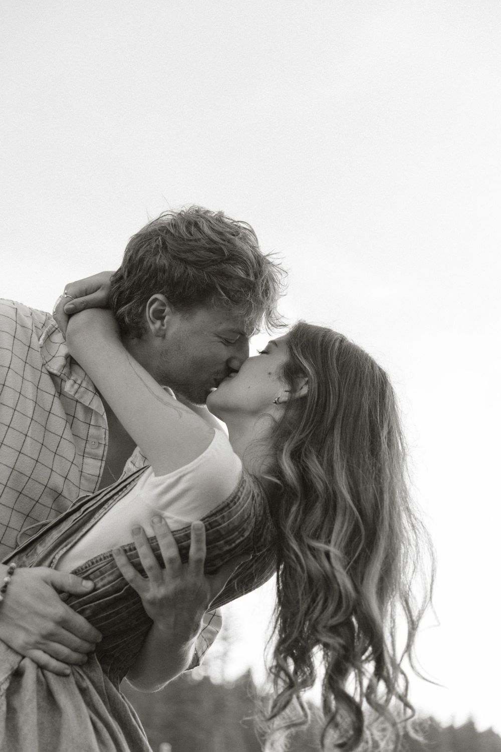 A romantic couple shares tender kisses in a series of black and white photographs against a fence.