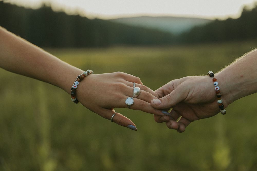 Two hands reach towards each other against a blurred natural outdoor background in romantic gesture.