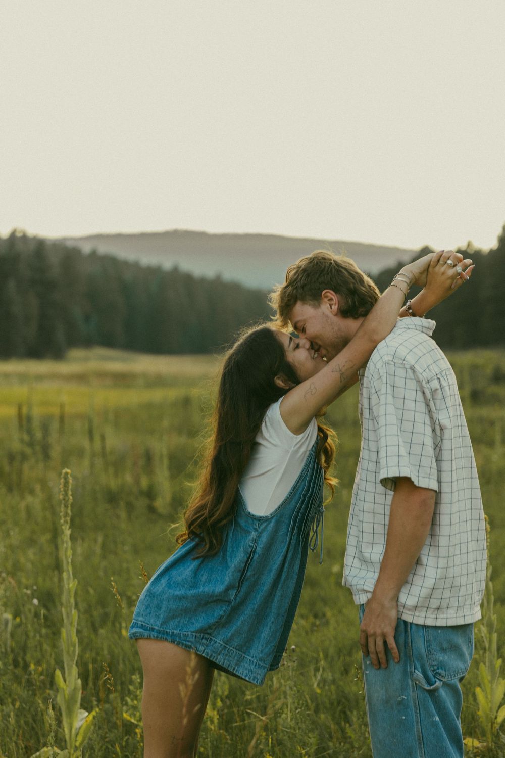 A tender moment between a couple in a grassy field during golden hour with mountains in the background.