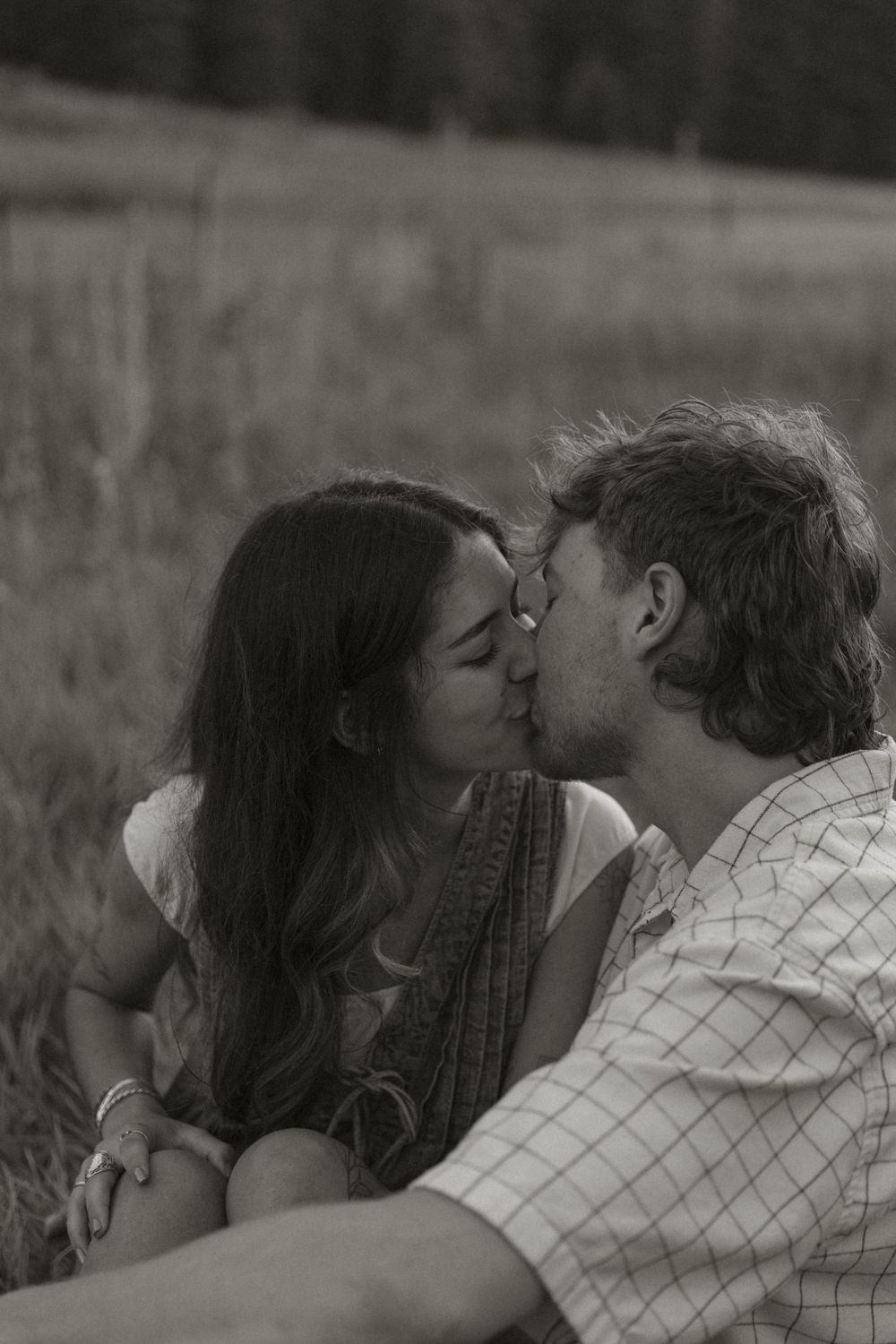 An intimate black and white portrait of a couple sharing a tender moment in a field.