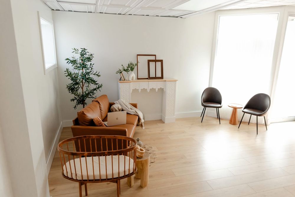 Bright minimalist living room with leather sofa, rattan chairs, wood floors, and neutral boho decor.