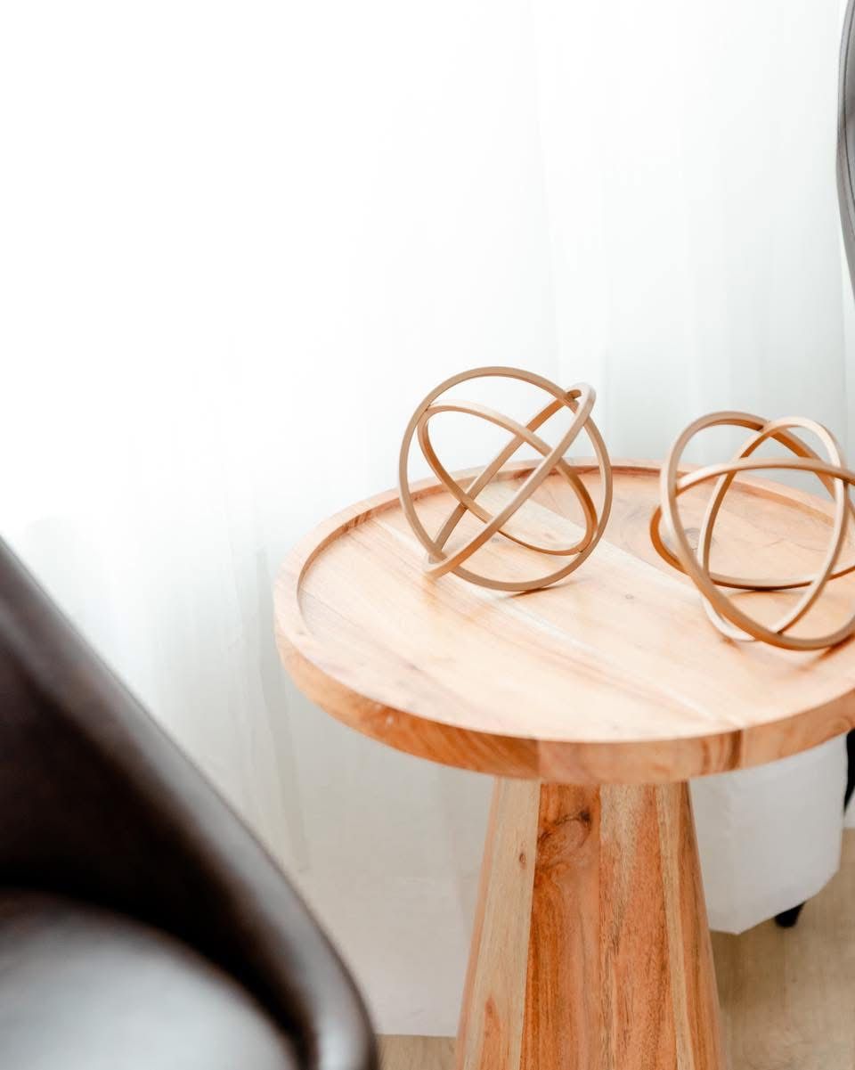 Two gold metal orb decorative spheres on a round natural wood side table in a bright minimalist living space.