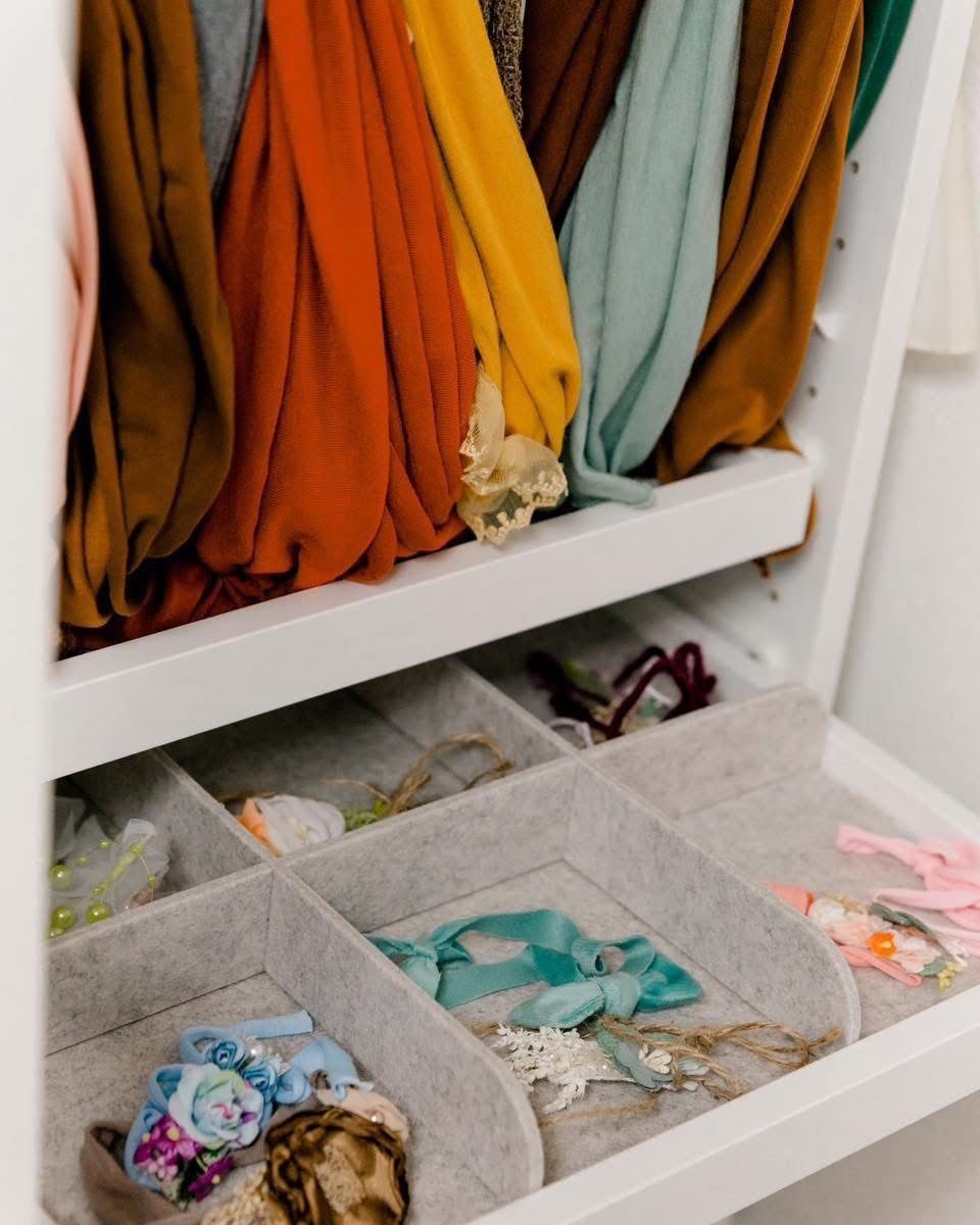 Organized closet drawer with felt dividers holding colorful hair accessories, scarves hanging neatly above.